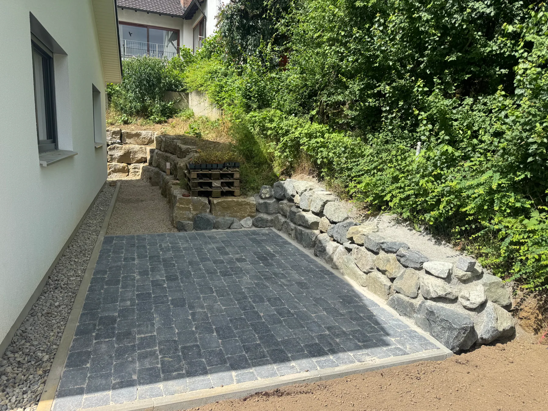 Gepflasterter Weg entlang eines Wohngebäudes mit seitlicher Steinmauer