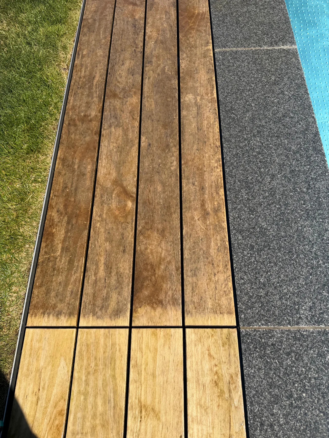 Terrassendetail mit Holzbelag neben Steinplatten und Rasen